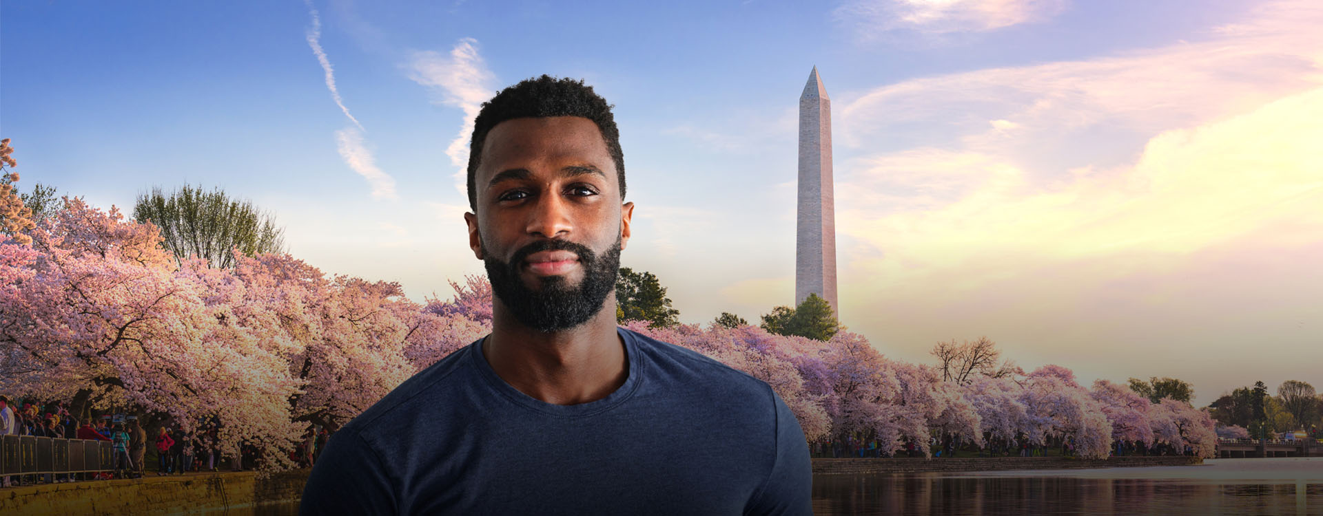 Hero Man standing in front of cherry blossoms at the Tidal Basin with the Washington Monument in D.C.